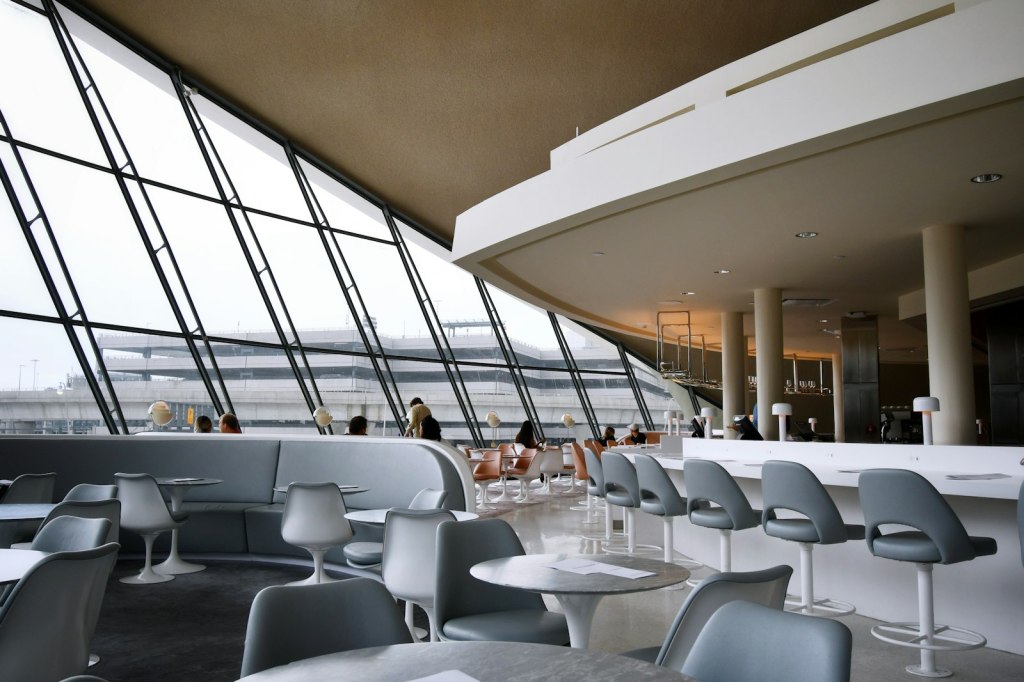Travelers relaxing in white chairs inside a bright airport lounge