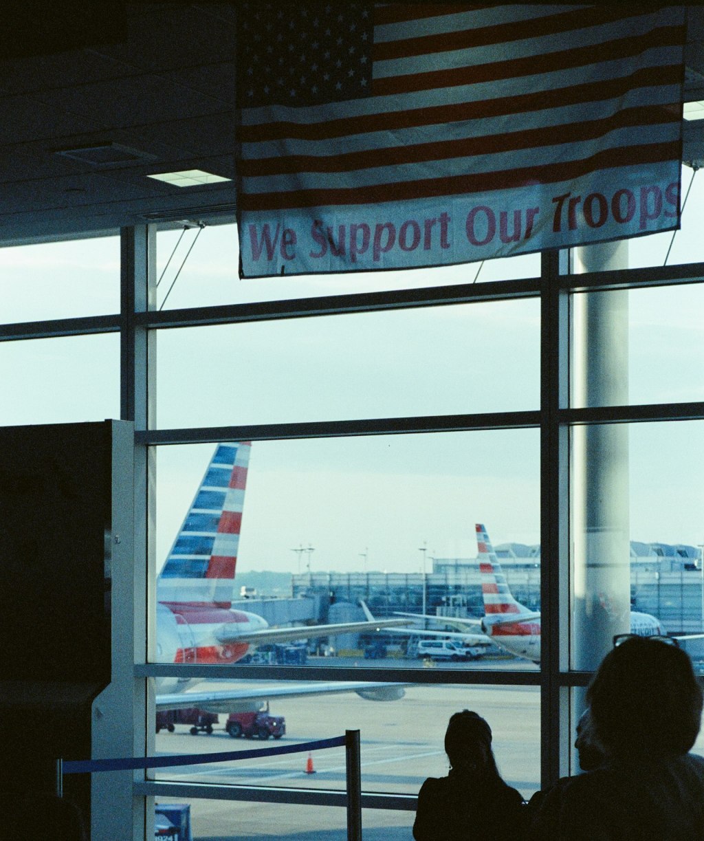 An American flag banner hanging inside an airport terminal with airplanes visible through the windows