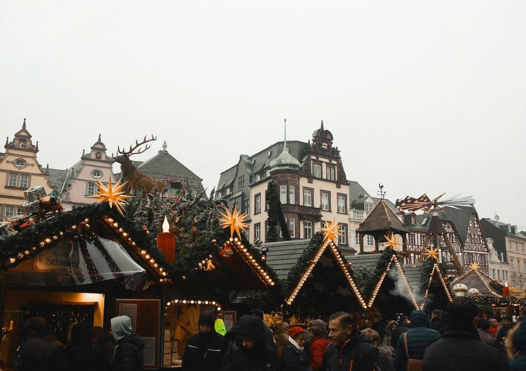 Shoppers walking past wooden Christmas market stalls dusted with snow in Trier, Germany