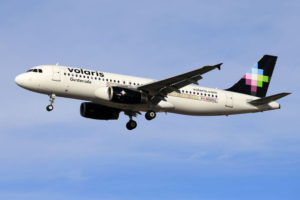 A Volaris passenger jet in flight against a clear blue sky