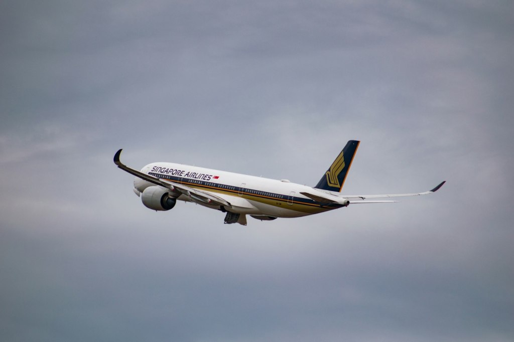A white Singapore Airlines passenger jet flying under a cloudy sky