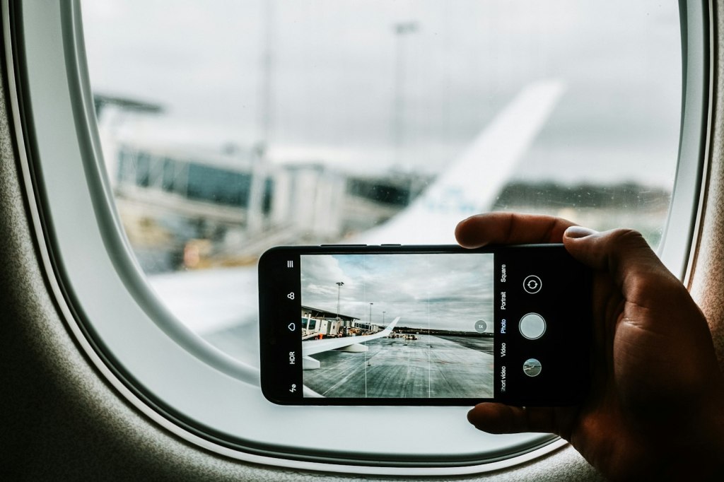 A black iPhone held up to photograph an airplane wing through an airport window