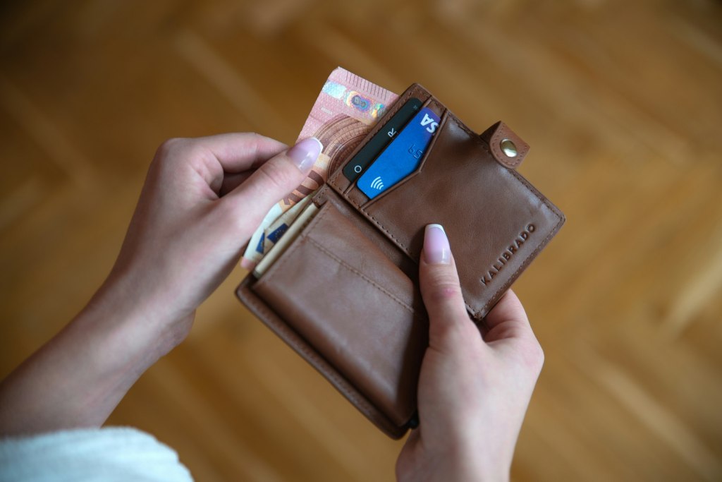 Hand holding a brown leather card wallet with several credit cards tucked inside