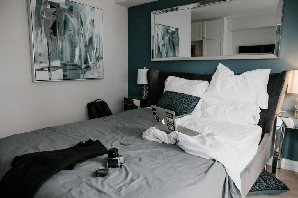 A black laptop open on a white bed in a hotel room