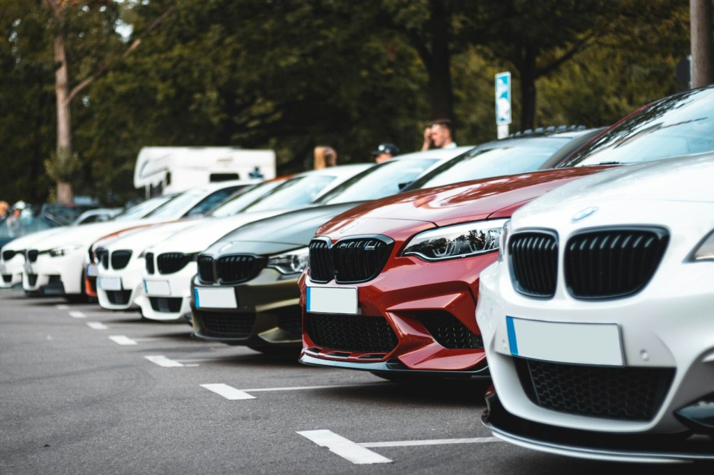 A row of parked white, olive and red sedans in a parking lot
