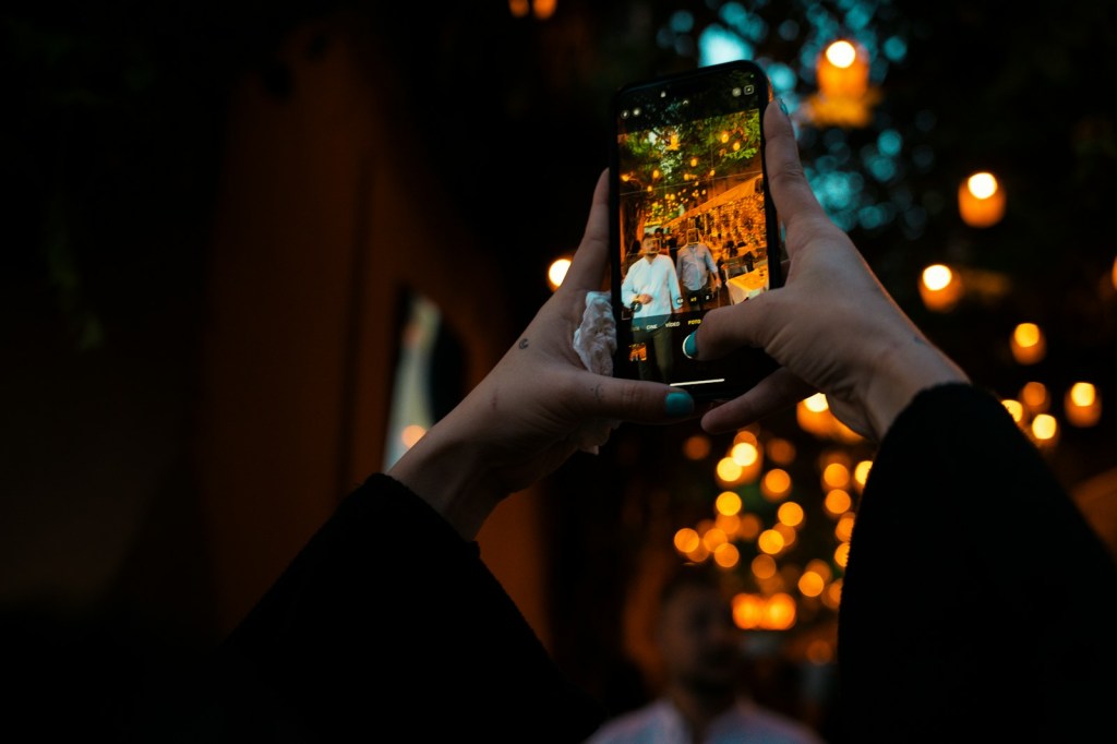 Hands holding a smartphone to take a photo on a lantern-lit street at night in Rome