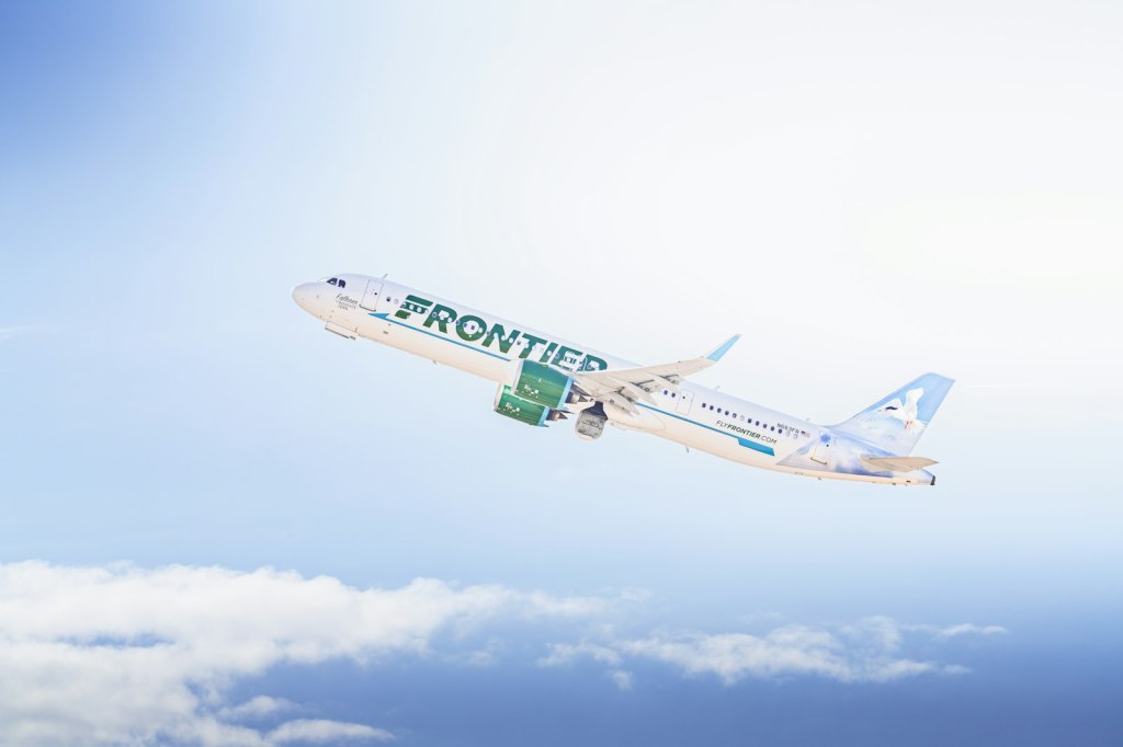 A Frontier Airlines plane climbing into a bright sky