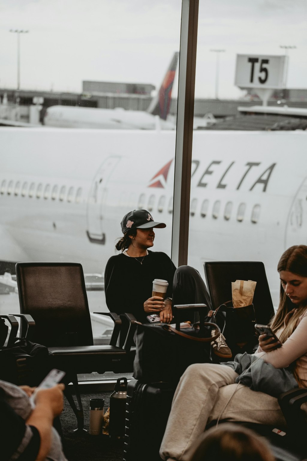 Traveler in a baseball cap holding a coffee cup at an airport gate before a flight