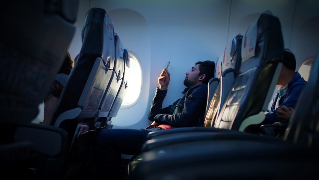 Traveler seated by an airplane window using a smartphone during a flight